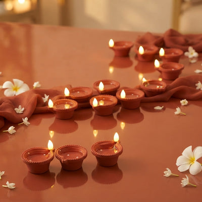 Twelve glowing LED sensor diyas arranged on a terracotta surface with burnt sienna decor, symbolizing mess-free festive light